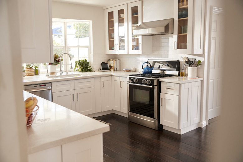 Domestic family kitchen with white furniture and dark wooden floorboards, seen from doorway