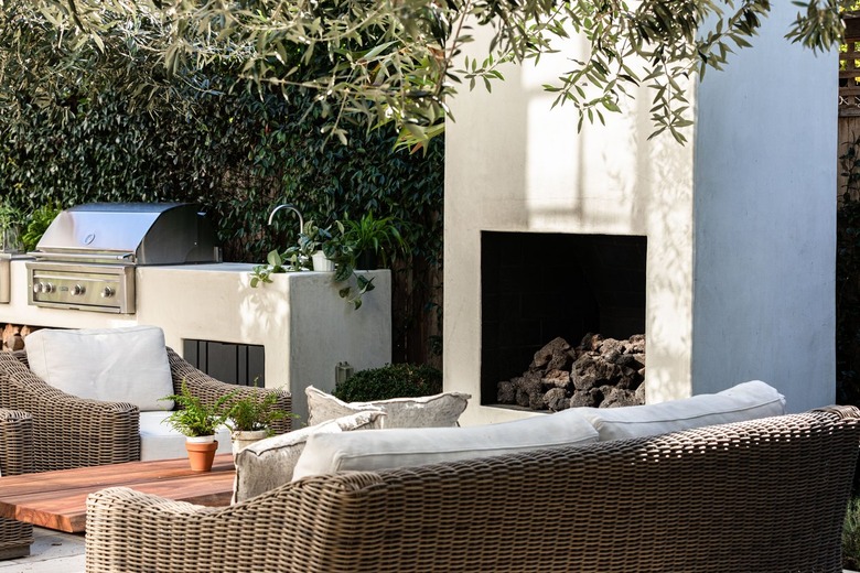 A patio with a fireplace, grill and white cushioned wicker seating