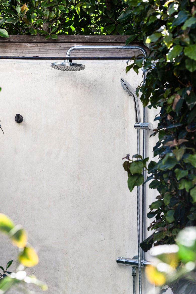 An outdoor shower by a white wall surrounded by ivy