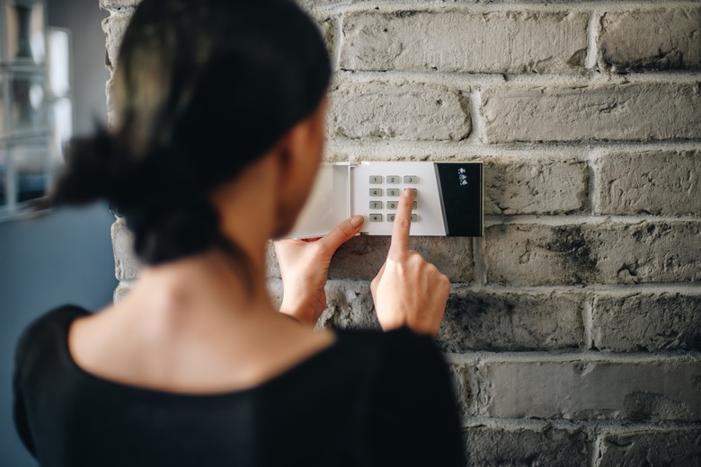 Young woman entering security pin on home alarm keypad.