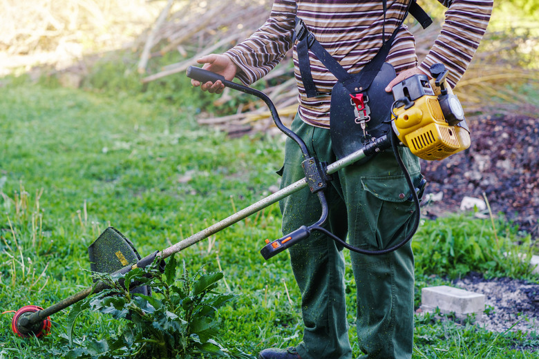 Midsection of unknown Young caucasian man farmer gardener standing in the field with string trimmer petrol Brushcutter ready to cut weed grass working on the farm cutting in the field in sunny day