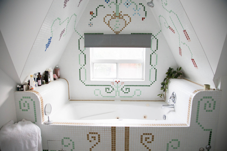 A-frame ceiling over a bathtub with mosaic floral and spiral designs, and a window.