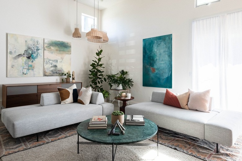 color scheme in modern-contemporary living room with couches, pillows, paintings, plant, and marble-top coffee table against white walls