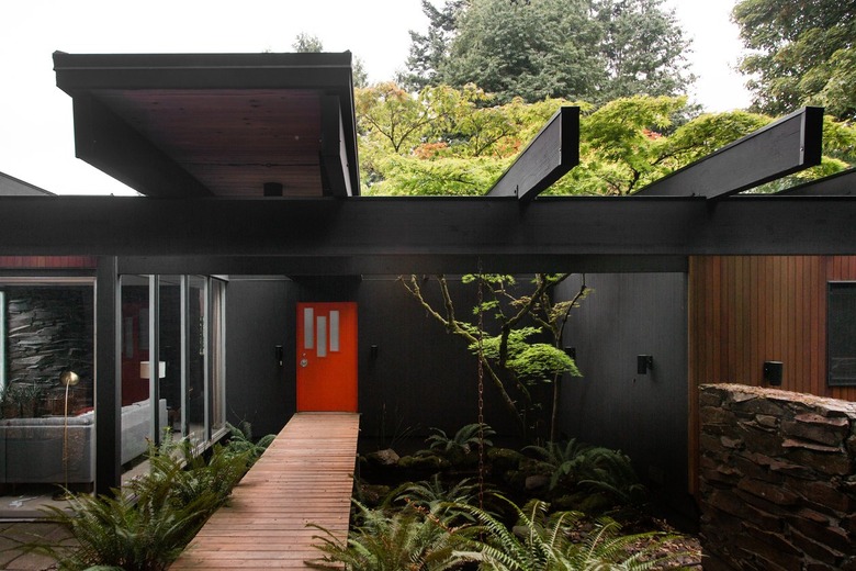 Contemporary black house with a plant lines wood walkway, leading to a red door.