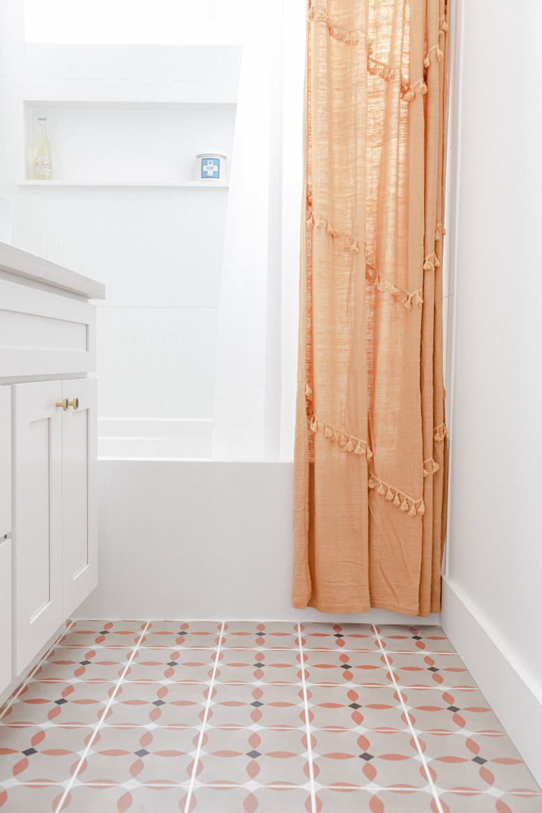 small bathroom with vinyl floor with orange, black and white pattern, white vanity, white bathtub, orange shower curtain