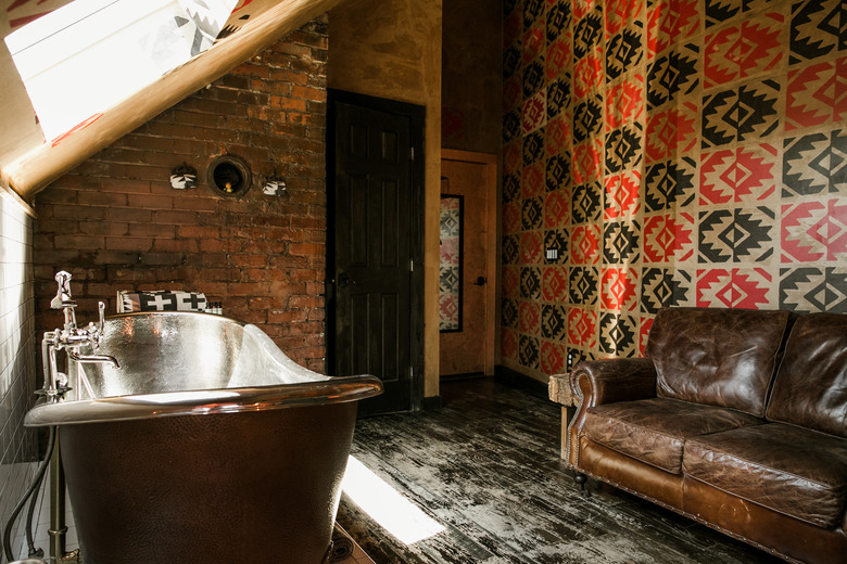 freestanding copper bathtub, distressed black wood floors, exposed brick walls, patterned red and black walls, leather couch