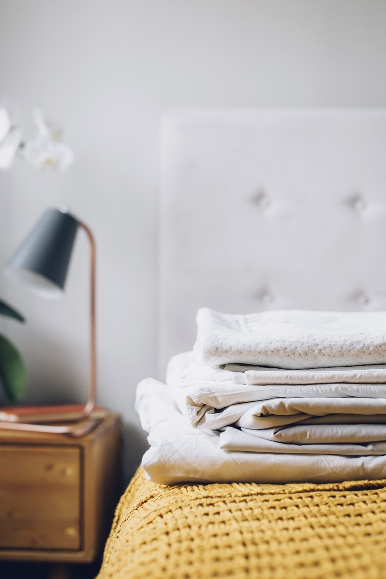 Folded white bed sheets on a bed next to a wood night stand with lamp