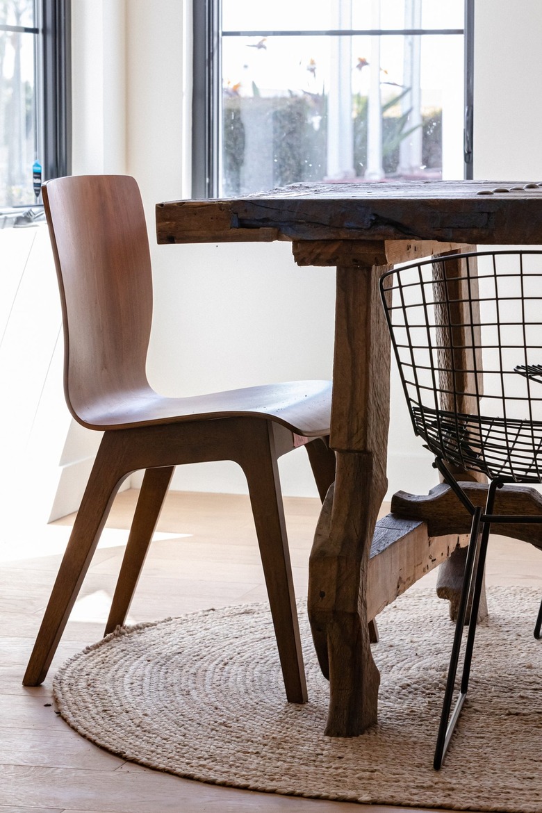 A wood chair and black wire chair at a wood dining table and a round jute rug