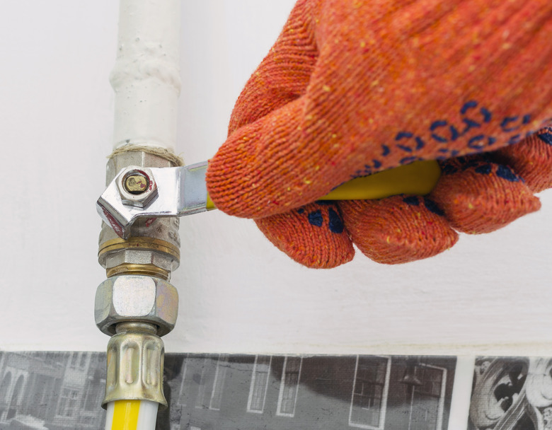 A gasman's hand in orange protective working gloves closes the gas valve.