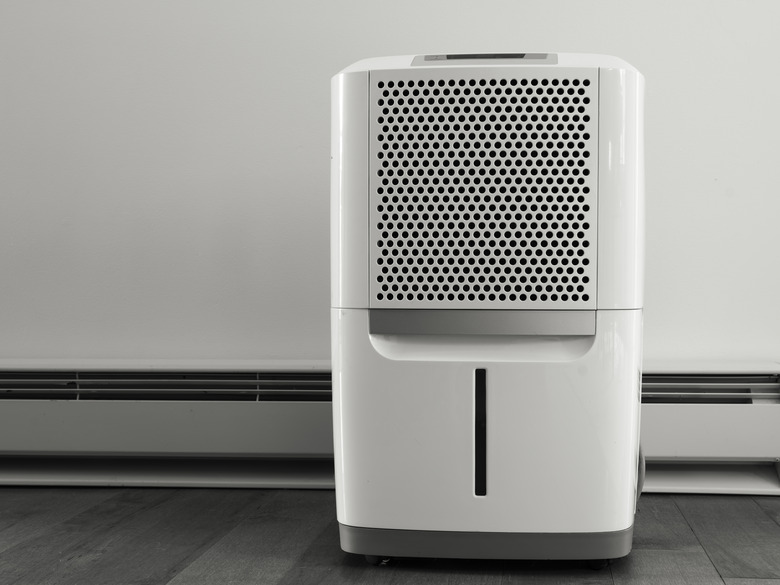 Portable white dehumidifier in front of electrical header installed over hard wood floor