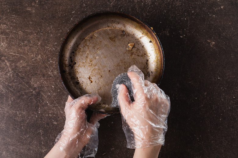 Wash the frying pan on a dark marble background. Hygiene. Wash dishes with gloves