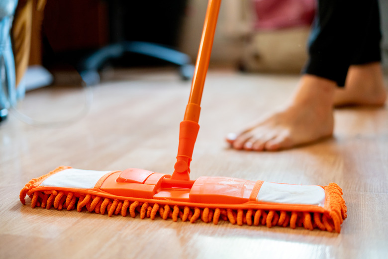 single man holding a mop and cleaning the laminate floor at home