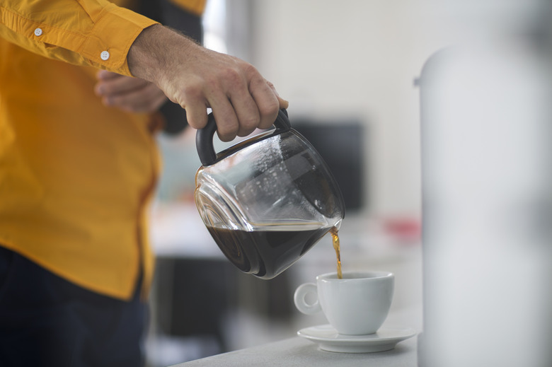 Employee with sling pouring coffee into cup at work