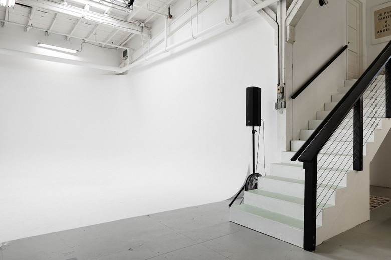 White stairwell leading down to concrete-floored room with tall ceiling and white walls.