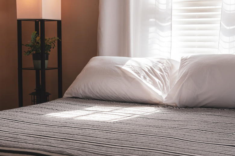 Morning sunlight streaming through white blinds in bedroom