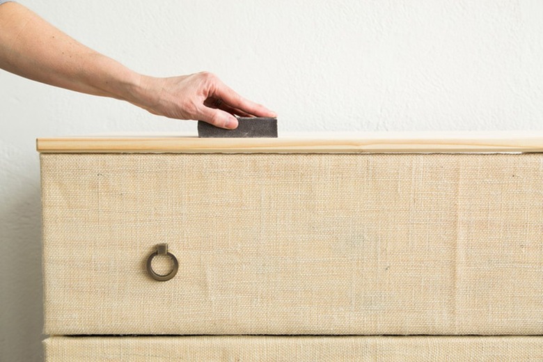 Person using a sanding block as prep for staining a pine wood Tarva dresser covered in burlap