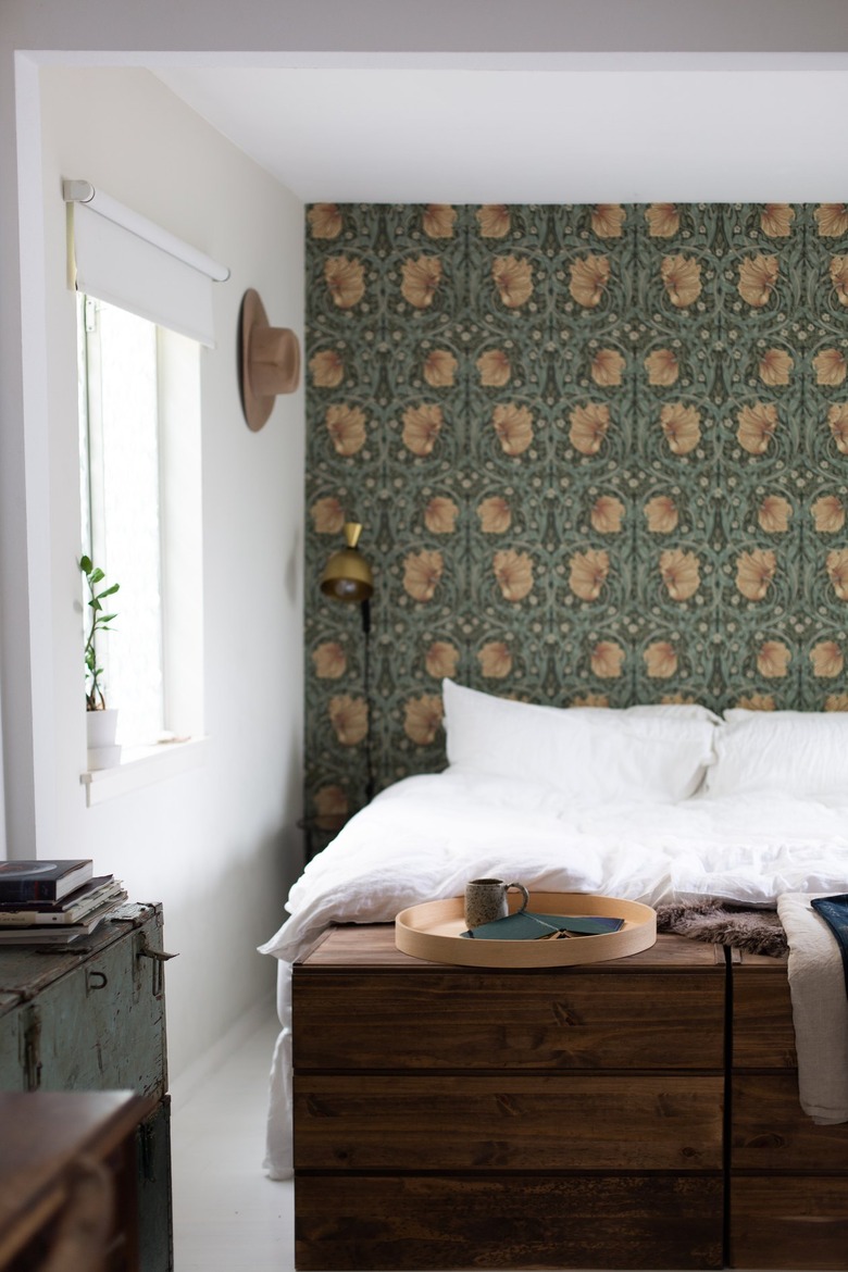 Bedroom with floral Art Nouveau wallpaper. A wood dresser, vintage trunk, and round wood tray.