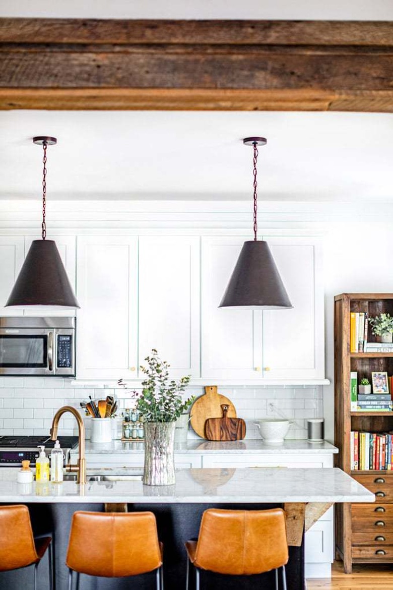 Rustic kitchen with exposed wood beams and distressed bookcase with leather counter stools