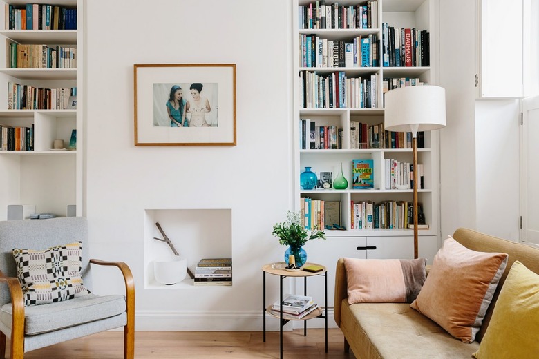 Modern living room with bookshelves, leather couch, chair, and small white fireplace underneath hung framed picture