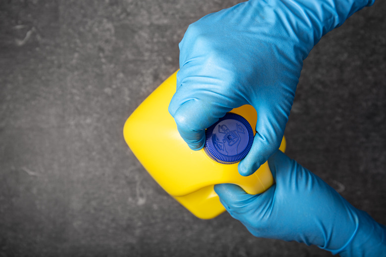 Human hand in protective glove opening a bleach bottle