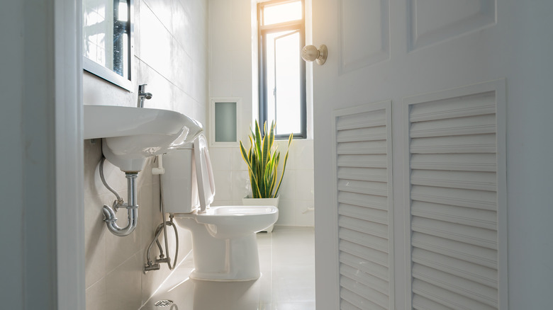 White bathroom door ajar with view of sink and toilet.