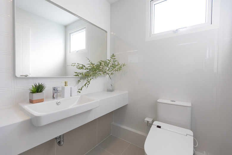 White bathroom with a toilet and sink with glass vase and green plant on counter