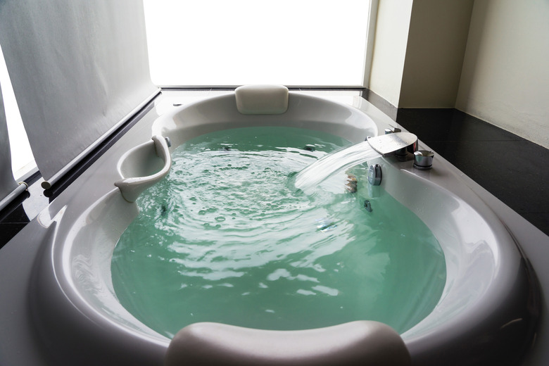 White massaging jetted bathtub with turquoise water and blank background