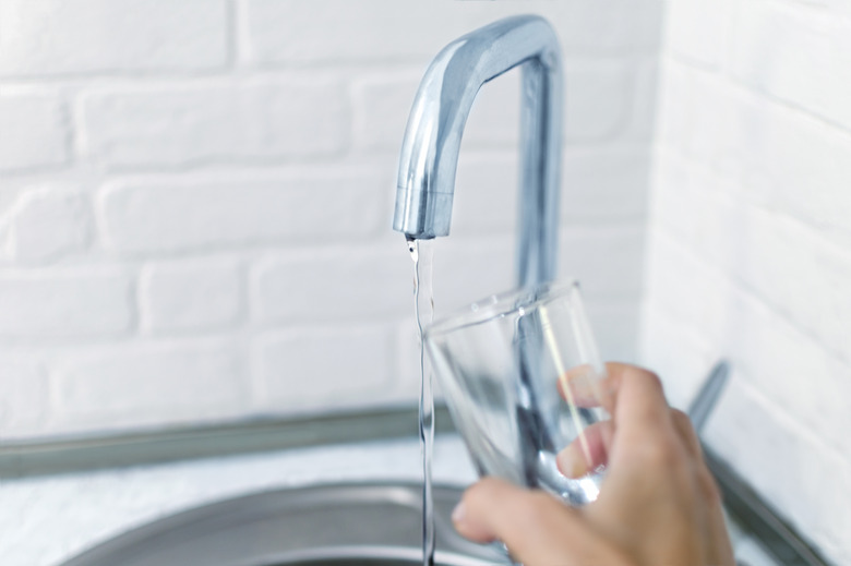 Women’s hand lifts the glass to the water jet from the faucet. Photo with hallow depth of focus.