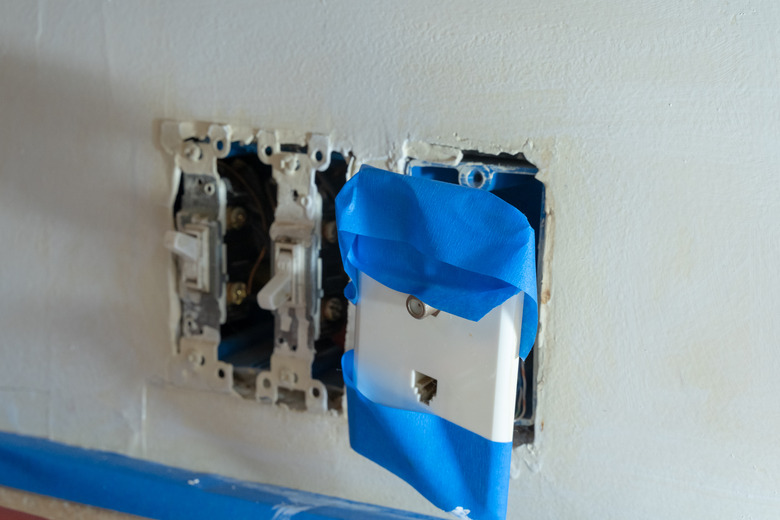 Electrical outlets (light switch, phone jack and cable) covered in painters tape with covers removed, due to home renovations and painting