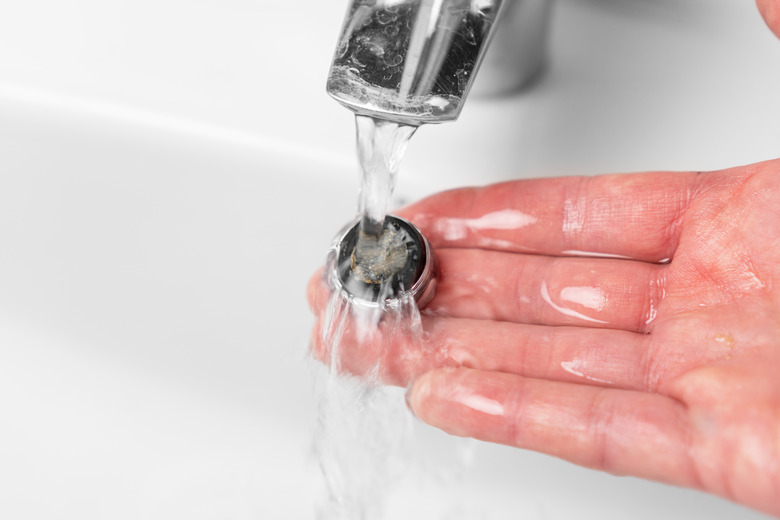 Washing the clogged filter aerator of a bathroom faucet sink with calcium sediments on the plumbers hand under running water. Plumbing repair