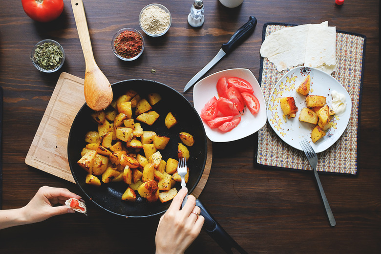 Girl eating baked potatoes in the oven with spices in a frying pan Homemade food. Rustic style. Organic vegetables, vegan and vegetarian recipe.