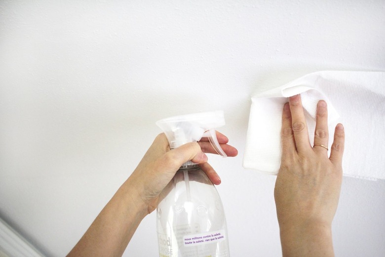 Cleaning a spot on the ceiling using a spray bottle and rag.