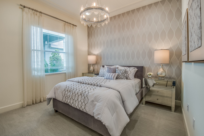 Bedroom with decorative wallpaper and sheer curtain panels.