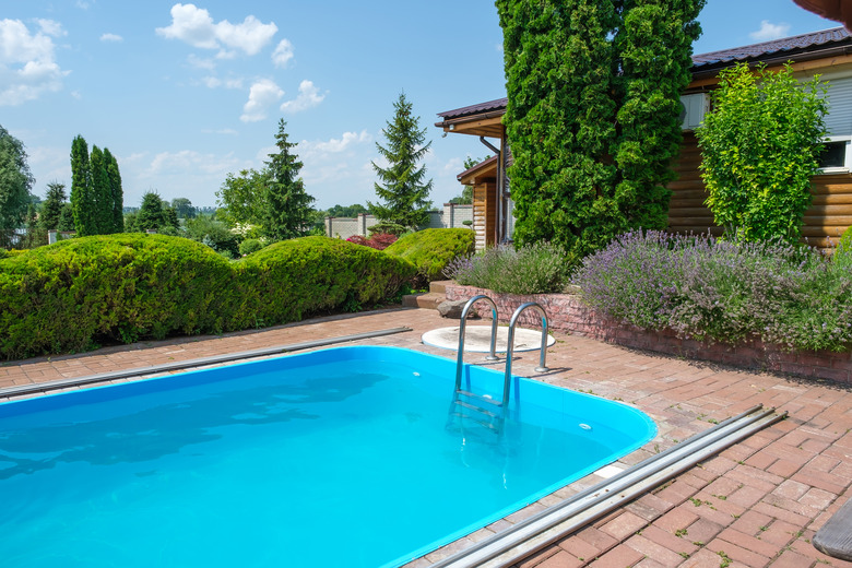 Swimming pool and garden with nicely trimmed bushes and stones in backyard.