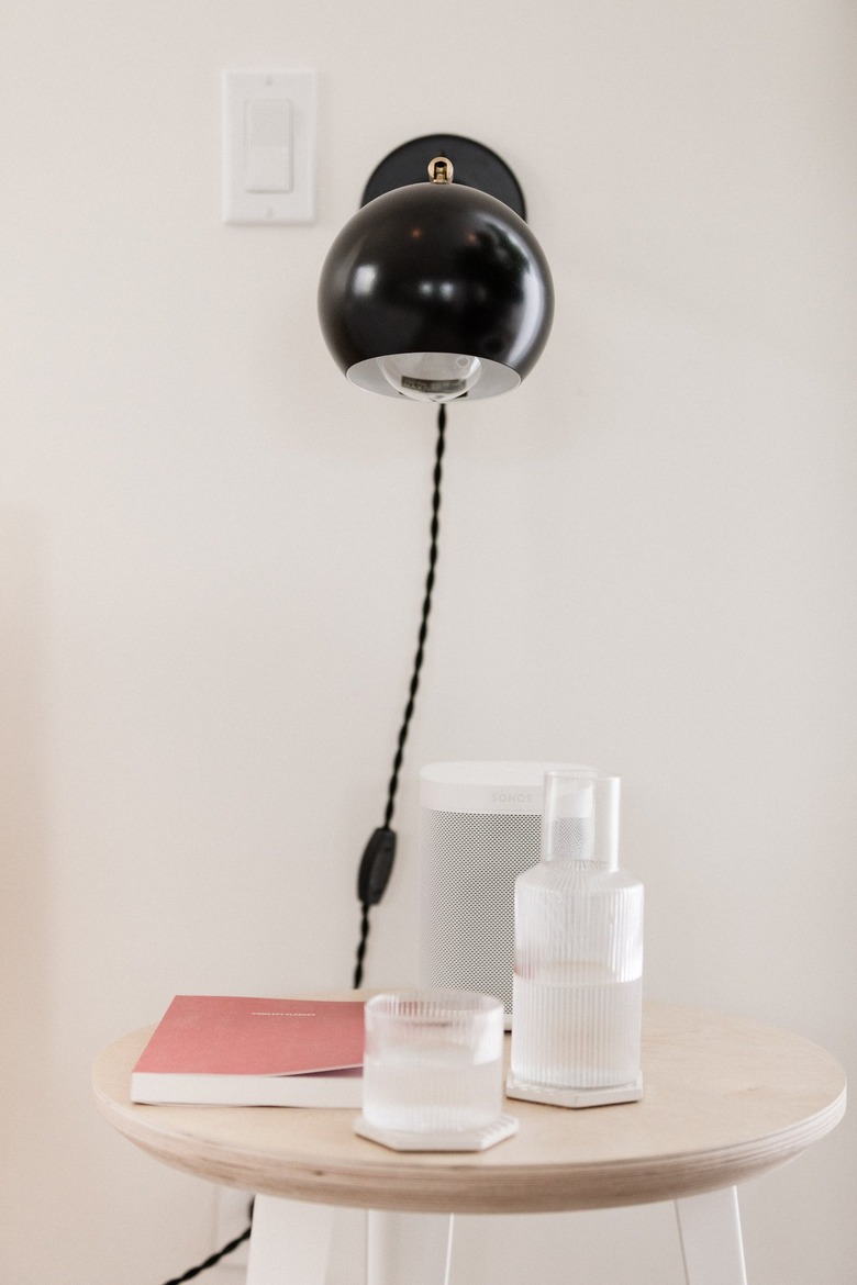 a glass decanter with a matching drinking glass, both on six-sided ceramic coasters under a long-armed wall sconce