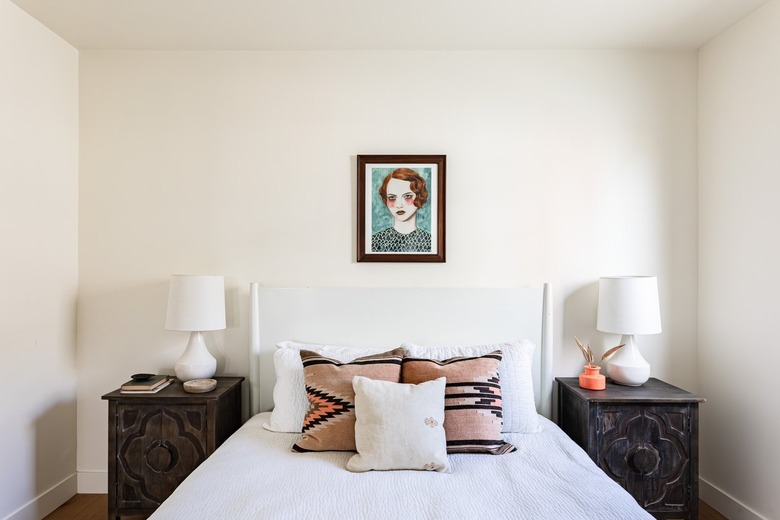 white bedroom white white bed, painting of red-haired woman, and dark wood nightstands