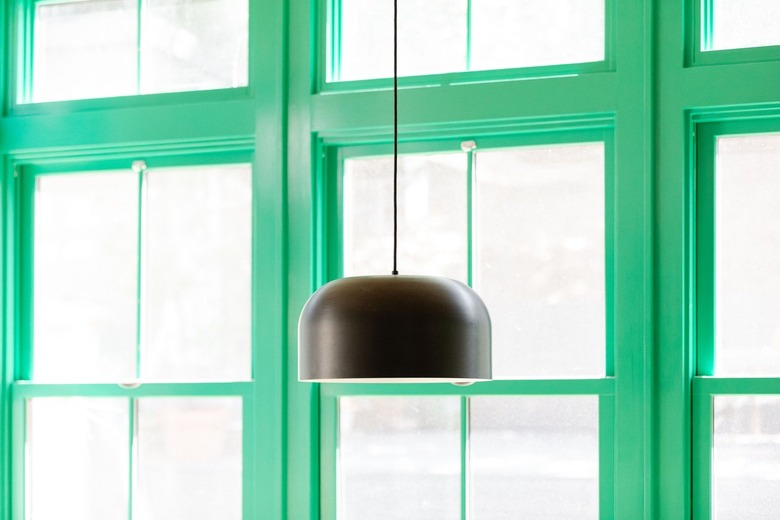 A brown hanging light fixture in front of green window frames.