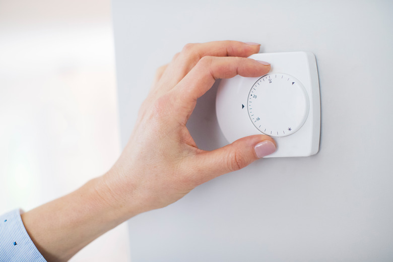 Close Up Of Female Hand On Central Heating Thermostat