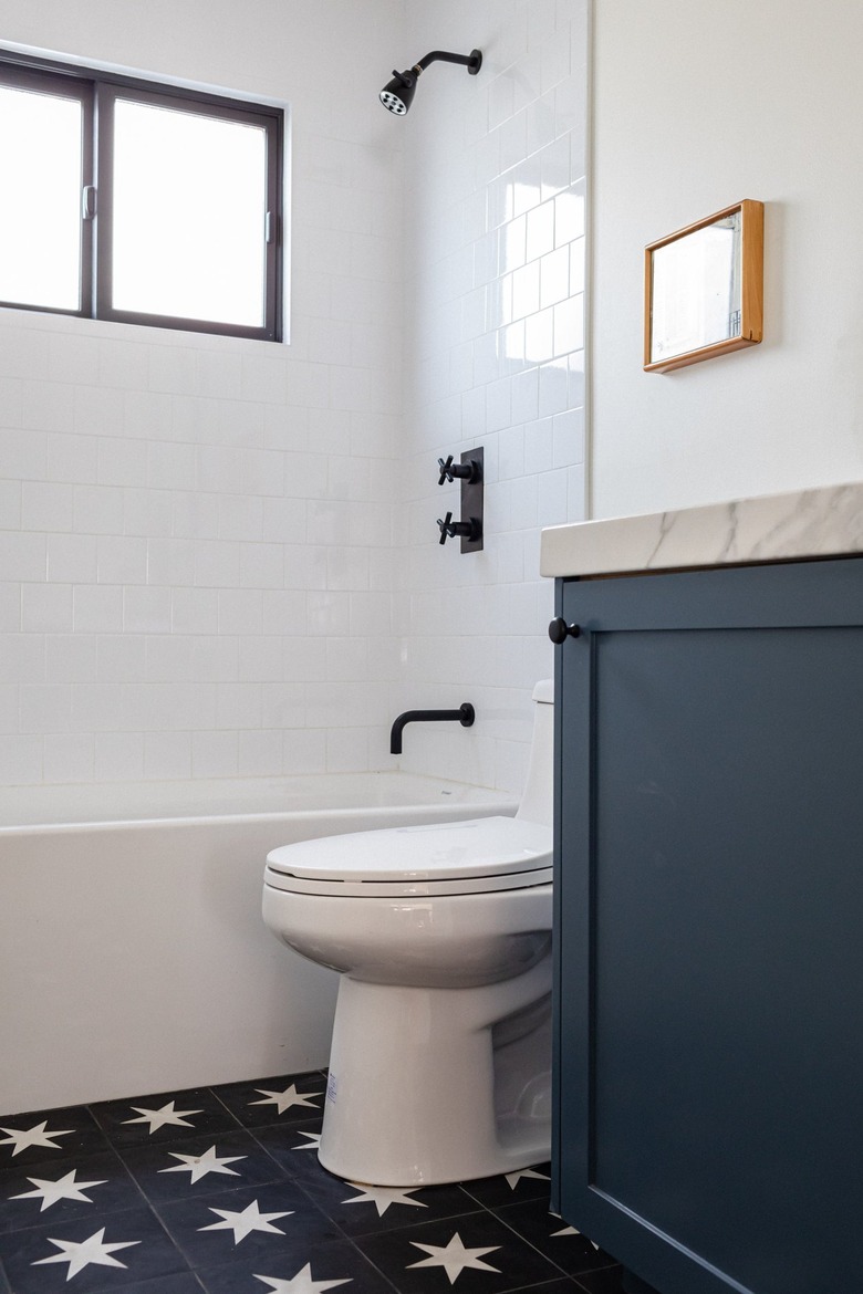 white toilet, blue vanity with marble countertop, blue tile floor with white star pattern, white bathtub, white subway tile, black faucet and showerhead, small window