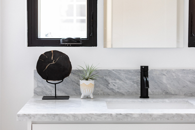 gray stone countertop, ceramic undermount sink, black faucet, window with black trim, white planter with green succulent, decorative black stone on a stand