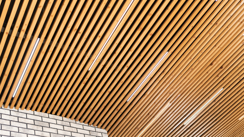 Loft style wooden plank ceiling design idea. Slatted wooden ceiling in the interior. Designer ceiling close-up. LED strip lamps in the design of a wooden ceiling.