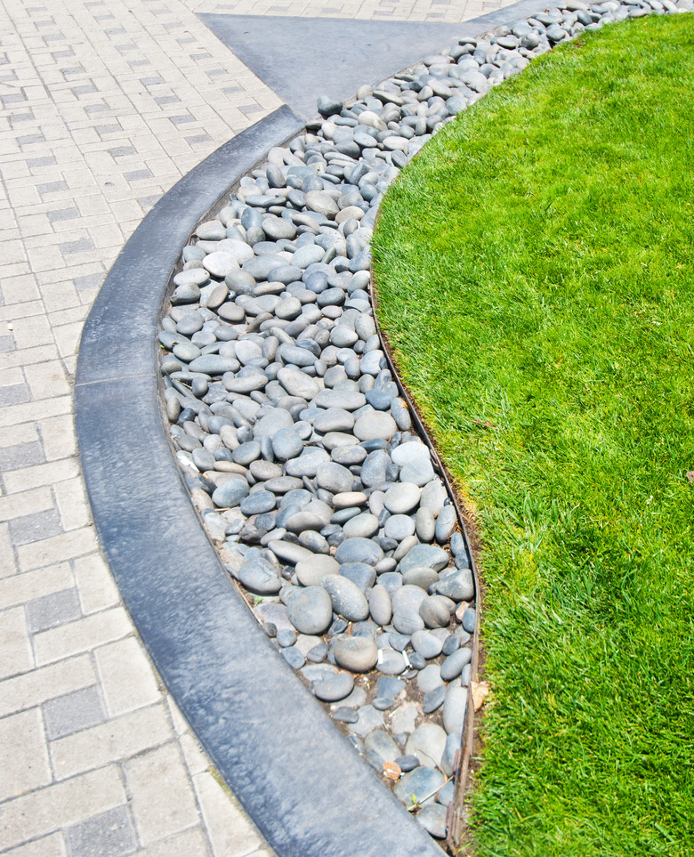 River rock stone border against fresh grass and paving bricks