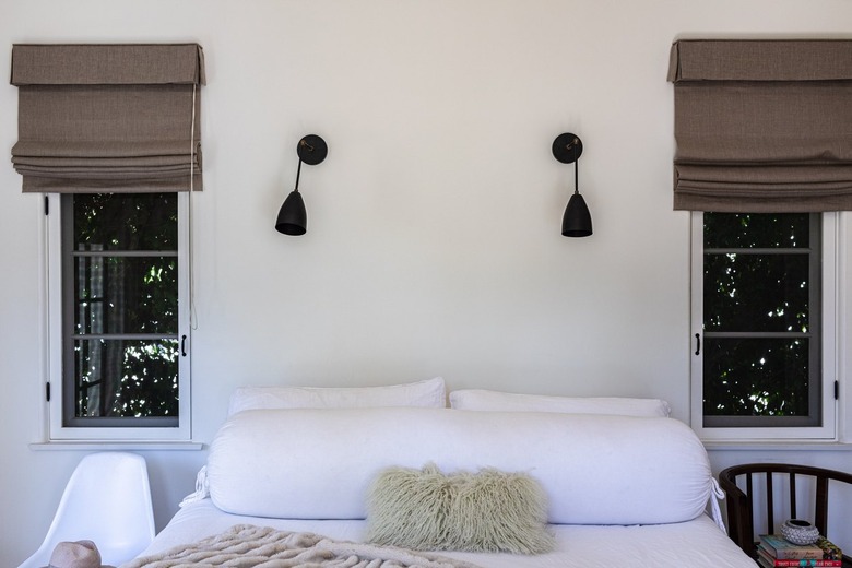 A bedroom with white bedding and windows with brown shades