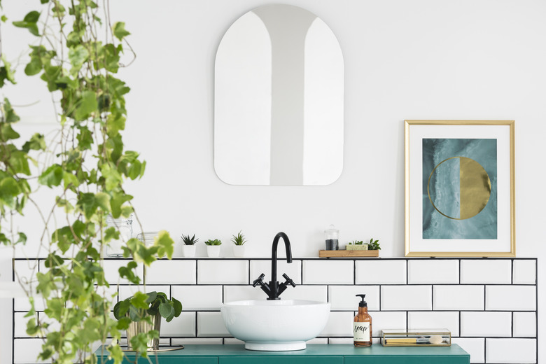 Mirror and poster in white bathroom interior with washbasin and plant. Real photo.