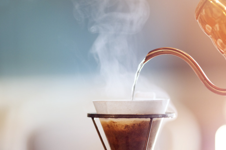 Barista pouring water on ground coffee in filter.