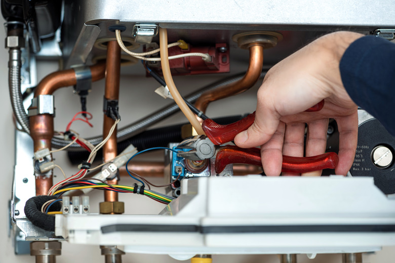 Technician repairing the combi gas boiler with wire cutter in hand