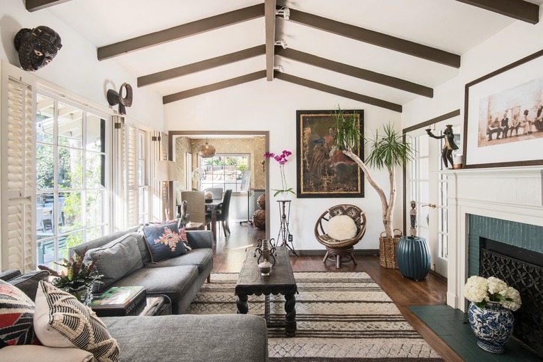 Wood beam ceiling living room with eclectic decor, gray sofa, flowers, wood coffee table, and wood-beige striped rug.