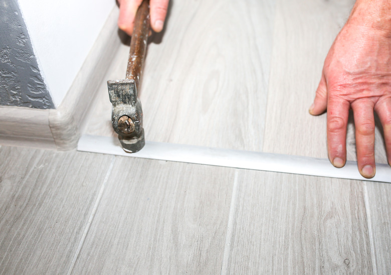 Installation of threshold indoors. Renovation works in the flat. Man with a hammer.