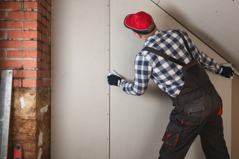 Man installing plasterboard sheet to wall for attic room construction