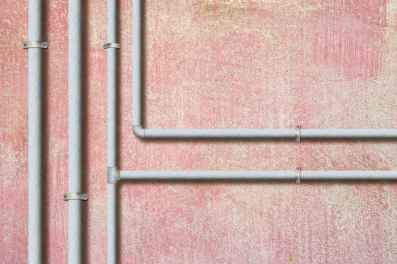 Water and gas galvanized metal pipelines in front of a plaster wall.